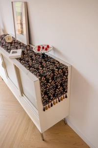 Floral table runner with orange patterns and multicolor tassels on a white cabinet