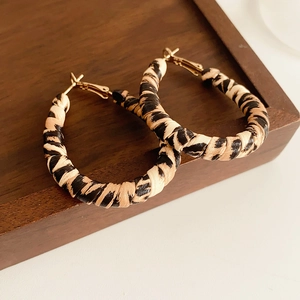 Macro detail of retro leopard print hoop earrings with textured fabric wrap on wooden tray