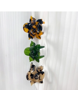 Three acetate flower hair claws in tortoiseshell and green colors on white fabric