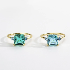 Detail view of square emerald-cut rings in green and aquamarine blue on white background