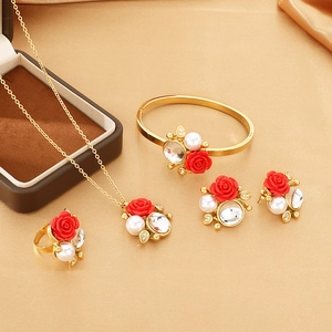 Detail shot of rose gold jewelry set with red roses and pearls on beige silk