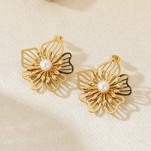 Detail view of gold hollow flower earrings with pearls on beige textured background