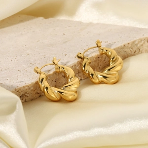 Detail of gold twisted hoop earrings resting on stone texture and silk fabric