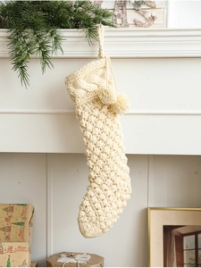 Detail of cream knit Christmas stocking with cable pattern and pom-poms on a fireplace