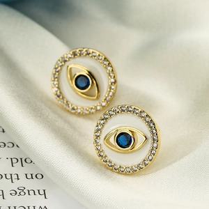 Macro shot of 18k gold plated evil eye stud earrings with blue zircon and white enamel