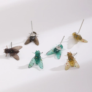Dettaglio macro di orecchini a forma di mosca in resina con glitter verdi e ambra