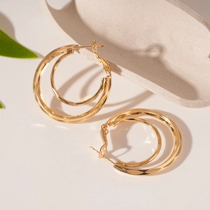 Close-up of double-layered geometric gold hoop earrings with textured outer ring detail