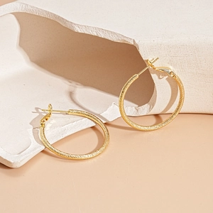 Detail of minimalist gold hoop earrings with matte textured finish on geometric prop