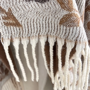 Detail of soft jacquard scarf showing brown leaf patterns and white fringe tassels