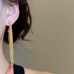Macro detail of long gold-plated waterfall tassel earrings worn by a model in soft light