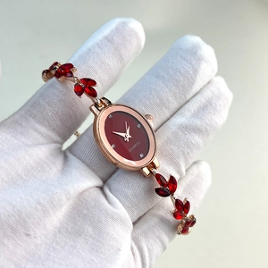 Detail view of oval gold watch with red dial and crystal leaf-shaped bracelet