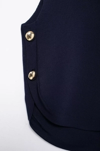 Detail of dark blue knitted vest featuring golden buttons and fine knit texture