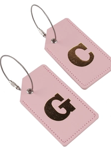 Two pink faux leather luggage tags with gold letters C and G and metal wire loops