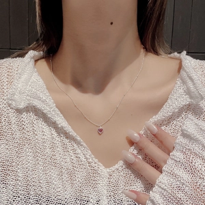 Close-up of a delicate silver chain with a translucent red heart pendant on a model