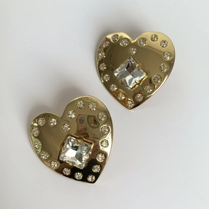 Close-up of golden heart earrings featuring a square center diamond and pavé rhinestones