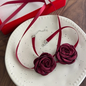 Elegant burgundy ribbon choker necklace with fabric roses on a white ceramic tray