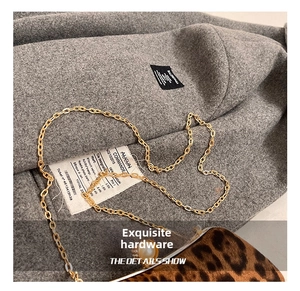 Détail macro du sac à imprimé léopard avec chaîne dorée et fermoir perle sur tissu gris