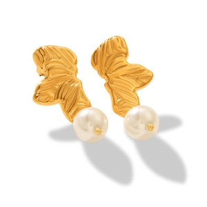 Detailed close-up of gold leaf-shaped earrings with hanging white pearls on white background