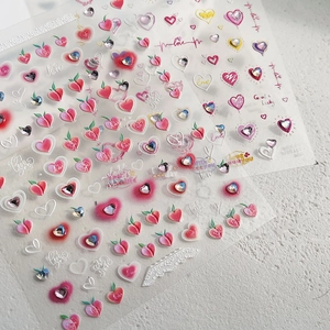 Macro shot of two nail art stickers with pink hearts, peaches and small rhinestones