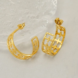 Golden C-shaped stainless steel earrings with hollow cross design on beige silk