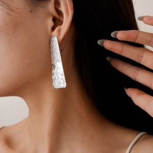 Detail of silver rectangular earring with textured hammered and radial finish