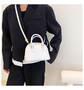 Detailed view of white quilted shell bag with gold hardware worn by a model