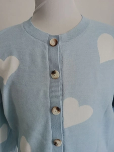 Detail of light blue knit cardigan featuring white heart patterns and tortoise buttons