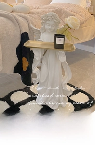 Detail of angel sculpture holding a golden metal tray with a black scented candle