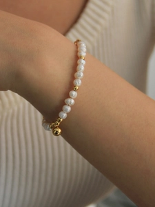 Détail d'un bracelet en perles d'eau douce avec billes dorées et pendentif sphérique