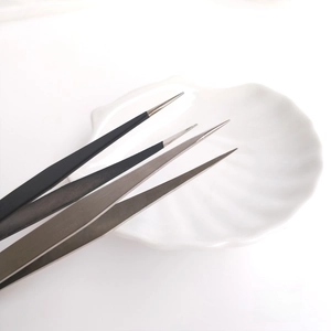 Precision stainless steel jewelry tweezers in black and silver on white decorative tray