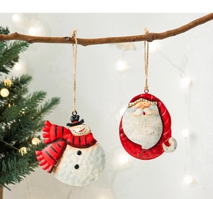 Detail of vintage painted metal Santa and snowman ornaments hanging on a pine branch