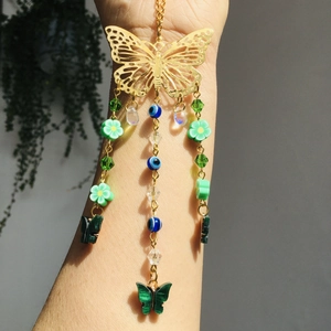 Detail view of a golden butterfly car charm with green beads and evil eye accents
