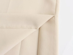 Detailed view of the beige woven fabric with fine texture and split hem stitching