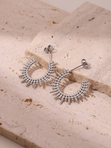 Macro view of silver sunburst C-shaped earrings on a textured beige stone background