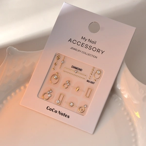 Close-up of golden geometric metal nail charms with diamonds on MJ-007 collection card