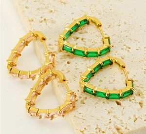 Detail of heart-shaped earrings with green and pink rectangular zircons on cream stone