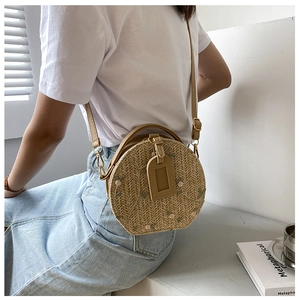 Detailed side view of beige round straw bag with floral embroidery on white summer outfit