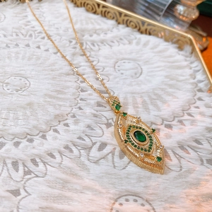 Macro shot of gold necklace with eye-shaped pendant set with green and white gemstones