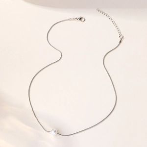 Detail of silver snake chain necklace featuring a polished white pearl and lobster clasp closure