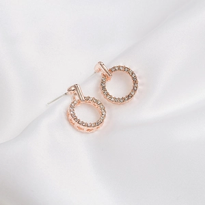Detailed view of rose gold round earrings with shimmering zircons on white silk backdrop
