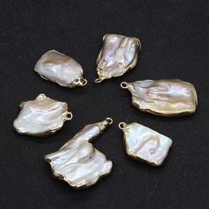 Detail of six baroque pearls with gold plated edges and loops on black texture