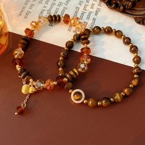 Détail de perles en œil de tigre et breloques de gourde dorées sur un fond de cuir