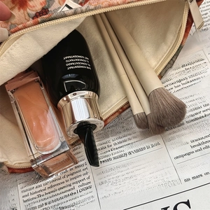 Close-up of leopard print corduroy makeup bag with skincare serums on vintage newspaper