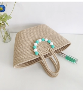 Detail of handmade beige straw tote bag featuring decorative white and teal pompoms