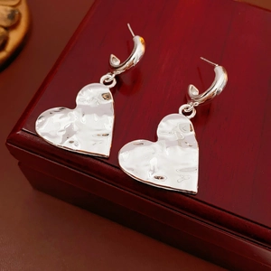 Macro detail of silver C-shaped heart earrings with hammered texture on wooden box