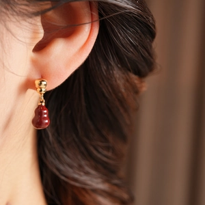 Macro detail of 18k gold plated earring with a smooth red gourd pendant on a model