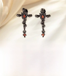 Macro detail of gothic snake cross earrings in black titanium steel with red zircon