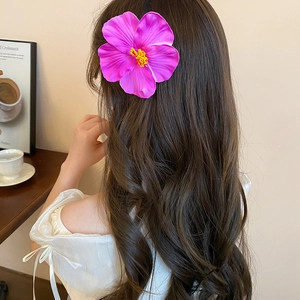 Detail of a large magenta hibiscus flower hair clip styled on wavy brunette hair