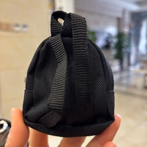 Close-up of a mini black nylon backpack keychain held between fingers for size reference