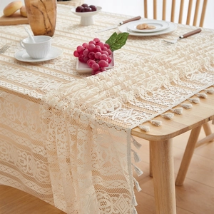 Detailed close-up of cream lace tablecloth with geometric hollow patterns and tassels